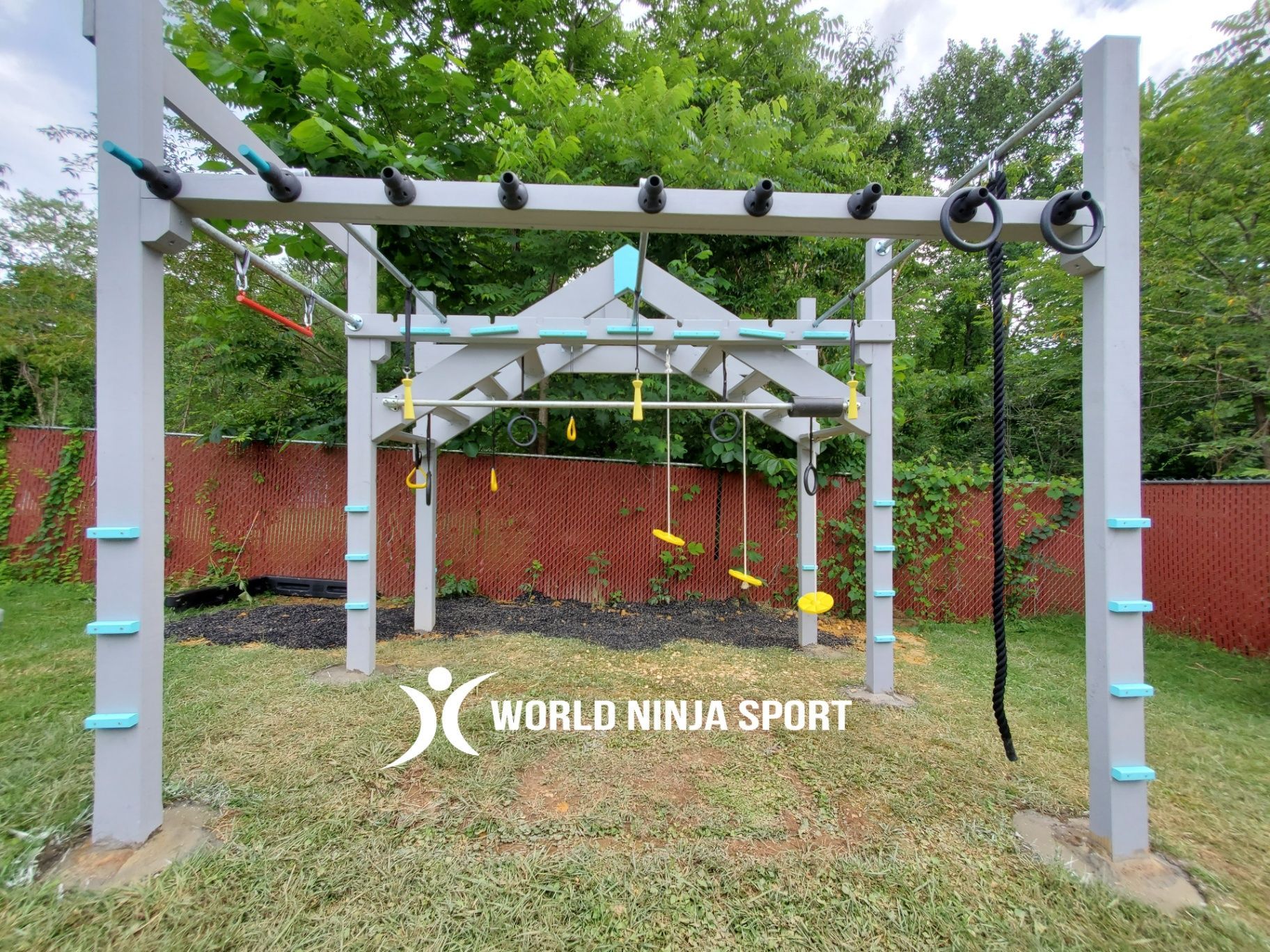 Outdoor ninja warrior obstacle course with a gray frame, hanging obstacles, rings, and a rope, set on a lawn.