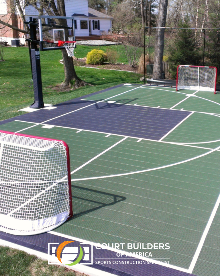 A backyard multi-sport court featuring green and dark blue tiles, a basketball hoop, and two hockey nets on a lawn.