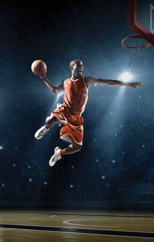 A basketball player in an orange uniform leaps to perform a slam dunk in a brightly lit arena.