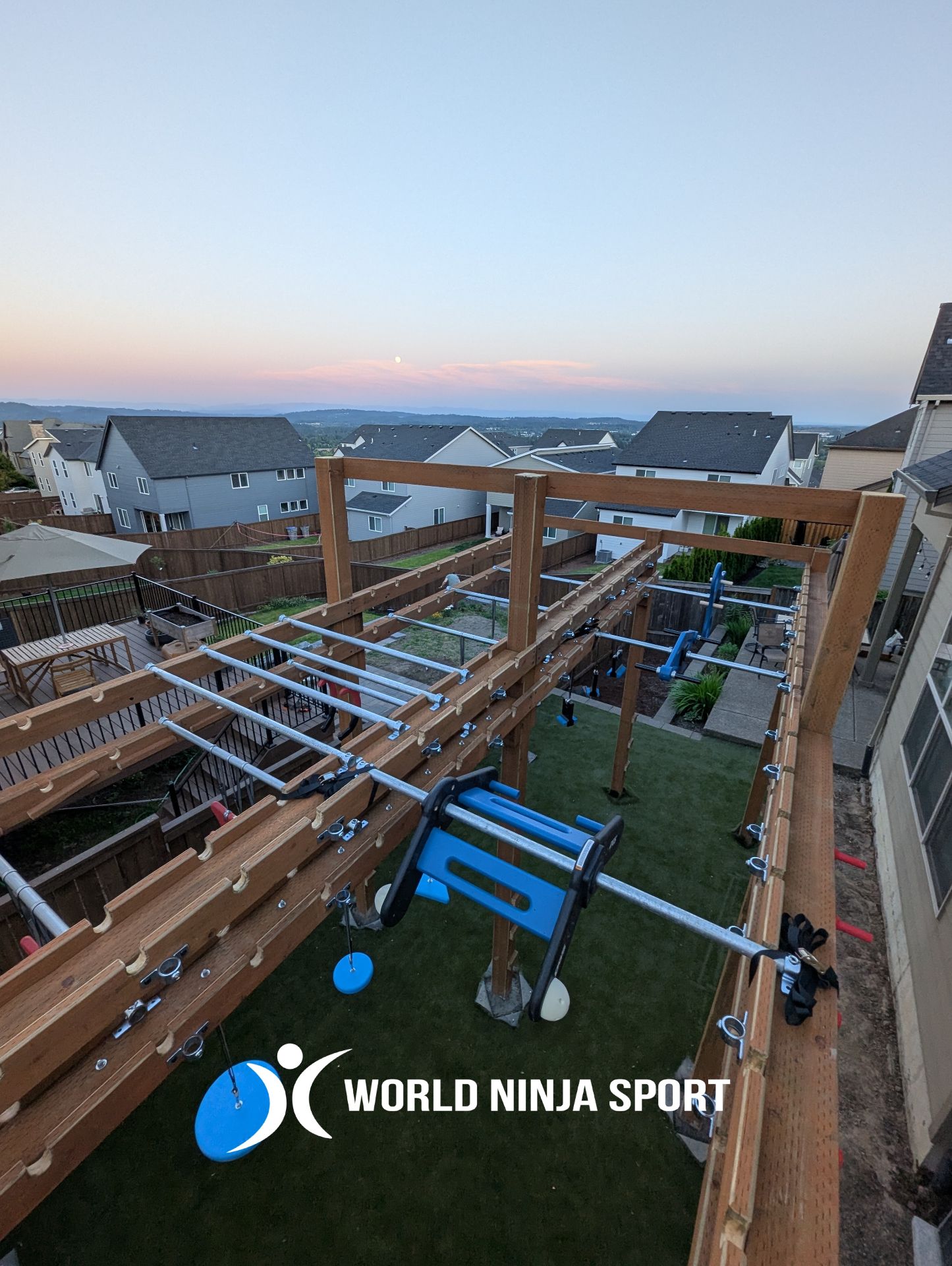 An outdoor wooden ninja warrior training structure featuring metal monkey bars and training equipment in a backyard.