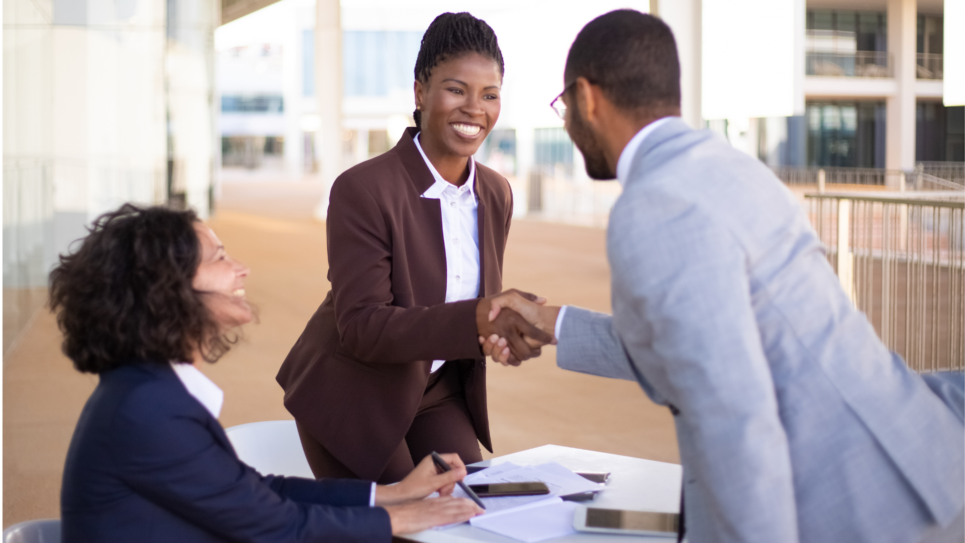 A man and a woman are shaking hands while sitting at a table.