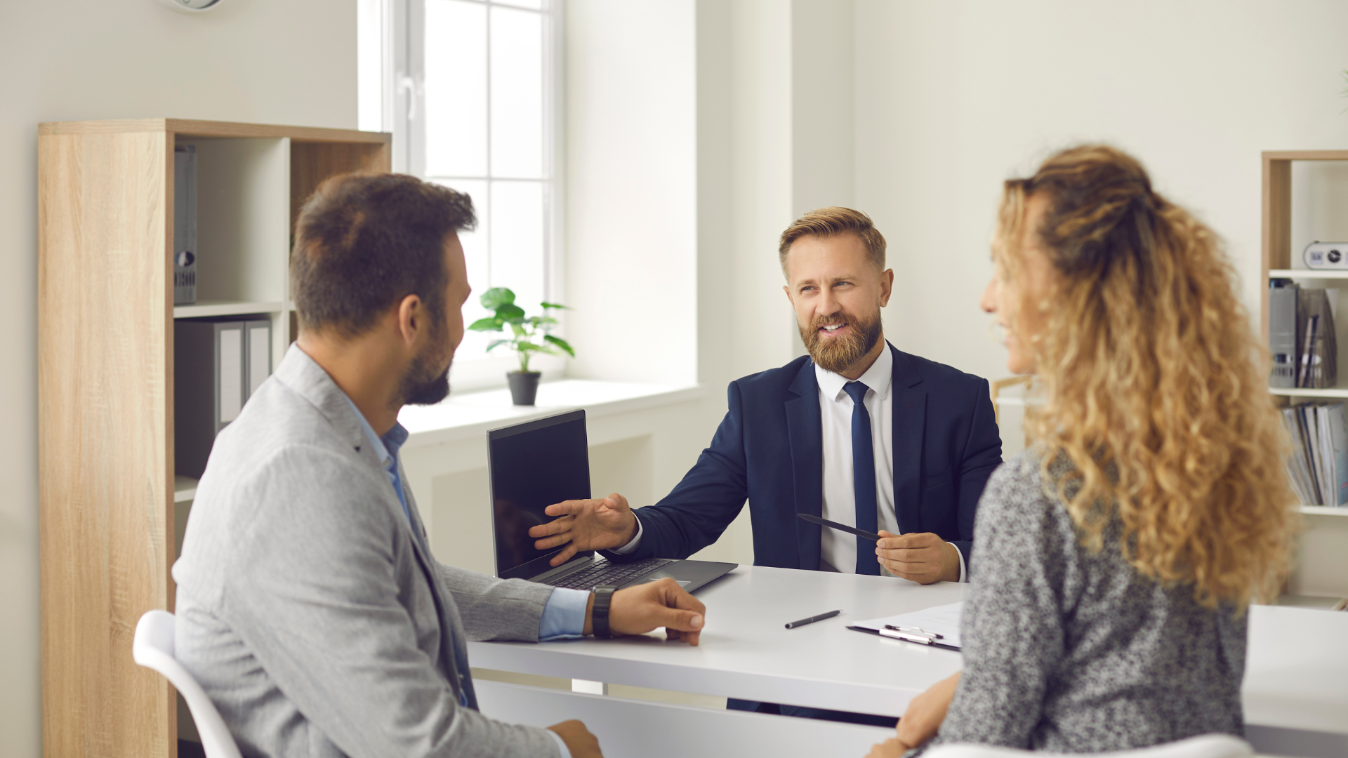 A man and a woman are sitting at a table talking to a man in a suit.