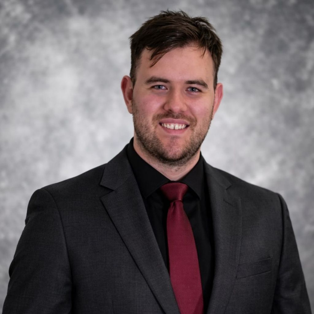 Man wearing a suit and tie, smiling at the camera, inside a building.