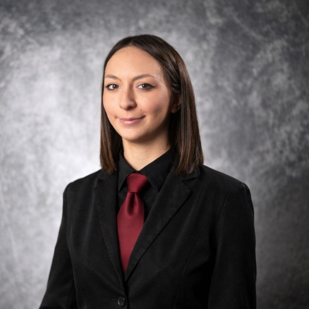 Woman in a black blazer and glasses smiles, wearing a name tag.