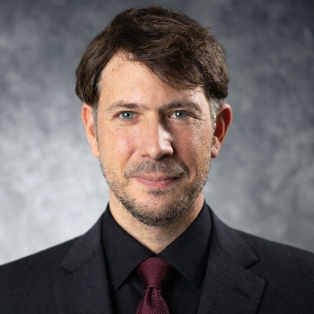 Woman in a black blazer and glasses smiles, wearing a name tag.
