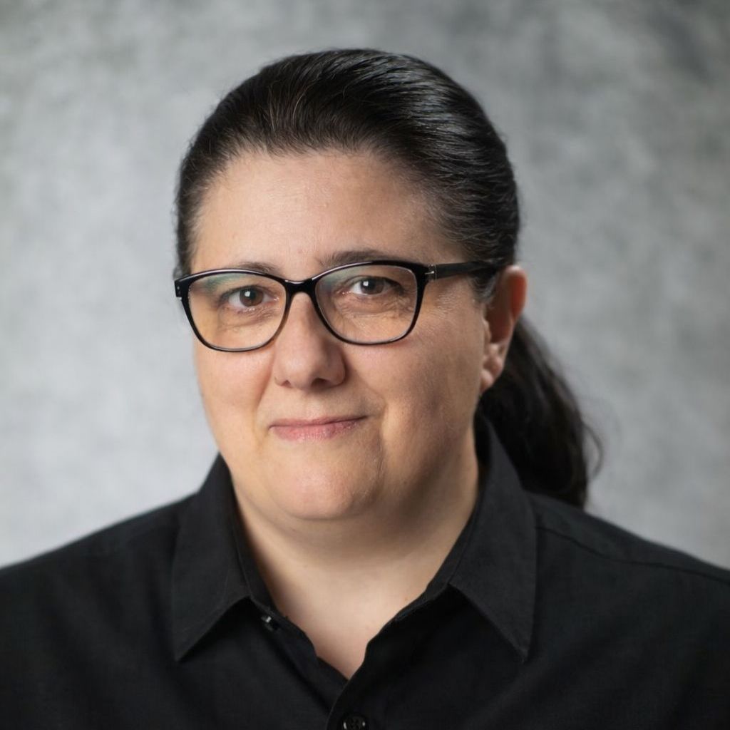 Smiling person in purple scrubs and a white hairnet.