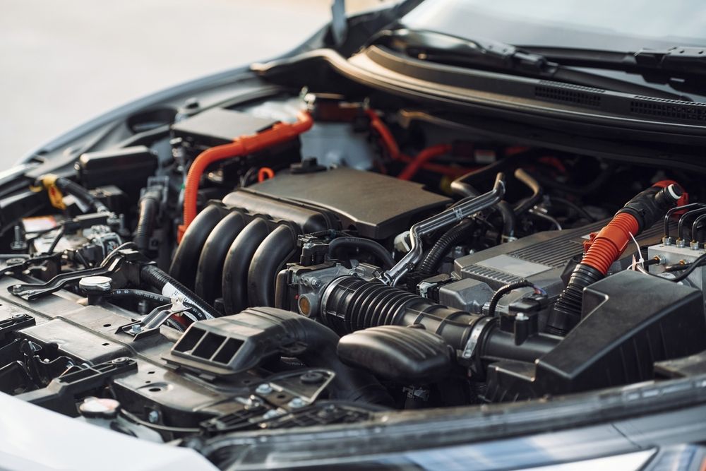 A detailed view of an open car engine bay, featuring black mechanical components and prominent orange high-voltage cables.