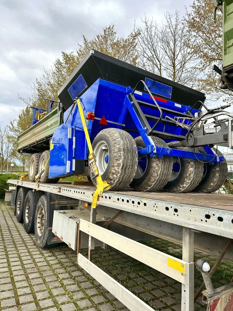 A blue agricultural fertilizer spreader strapped to a flatbed trailer outdoors on a paved lot.