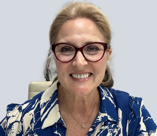 A woman wearing glasses and a blue shirt is smiling.