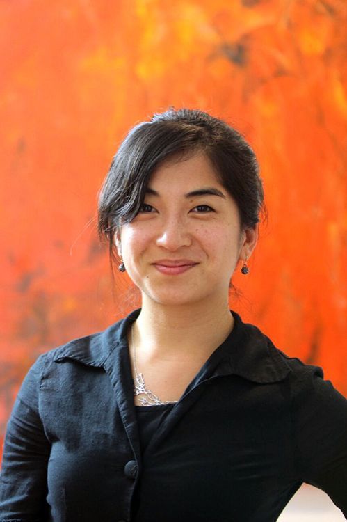A woman in a black shirt is smiling in front of an orange wall