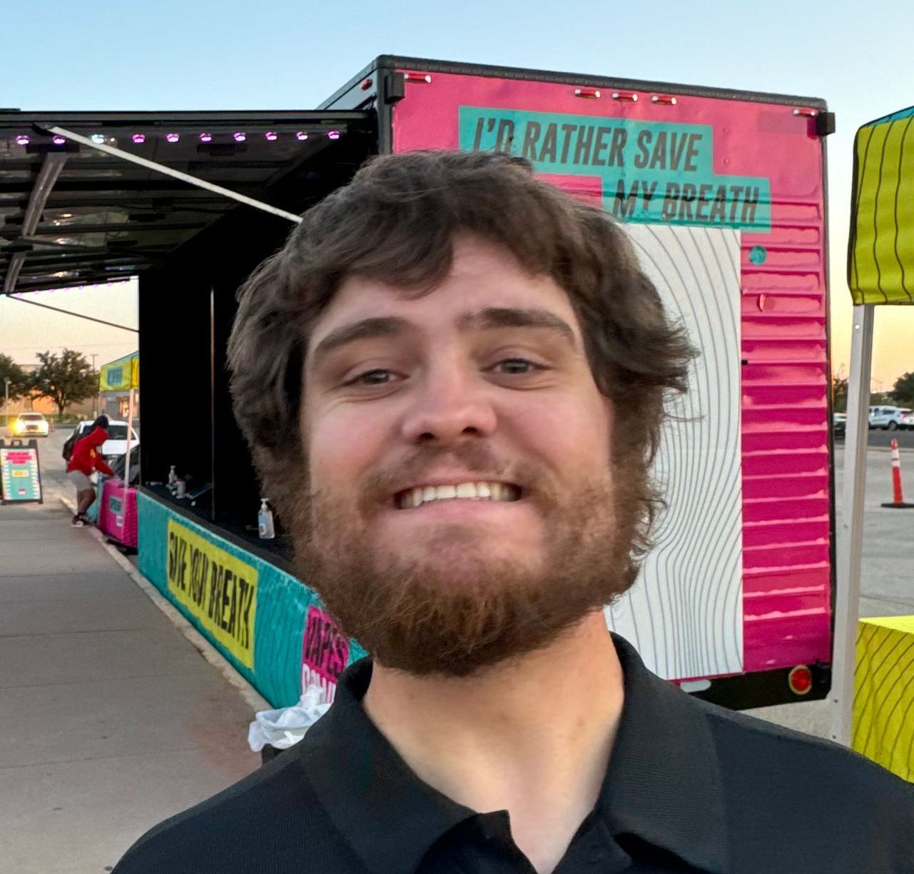 A man with a beard is smiling in front of a trailer that says i'd rather save my breath