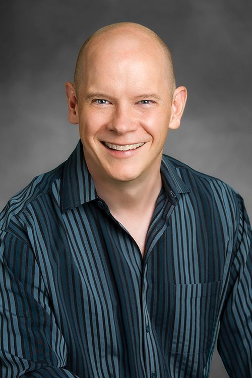 A smiling bald man wearing a blue striped shirt