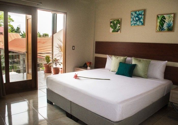 Dormitorio con una cama grande, balcón y arte vegetal enmarcado en la pared.