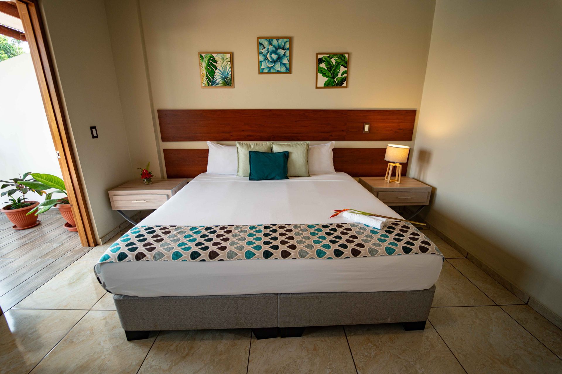 Dormitorio con cama, mesas de noche y arte mural; puerta a un patio a la izquierda.