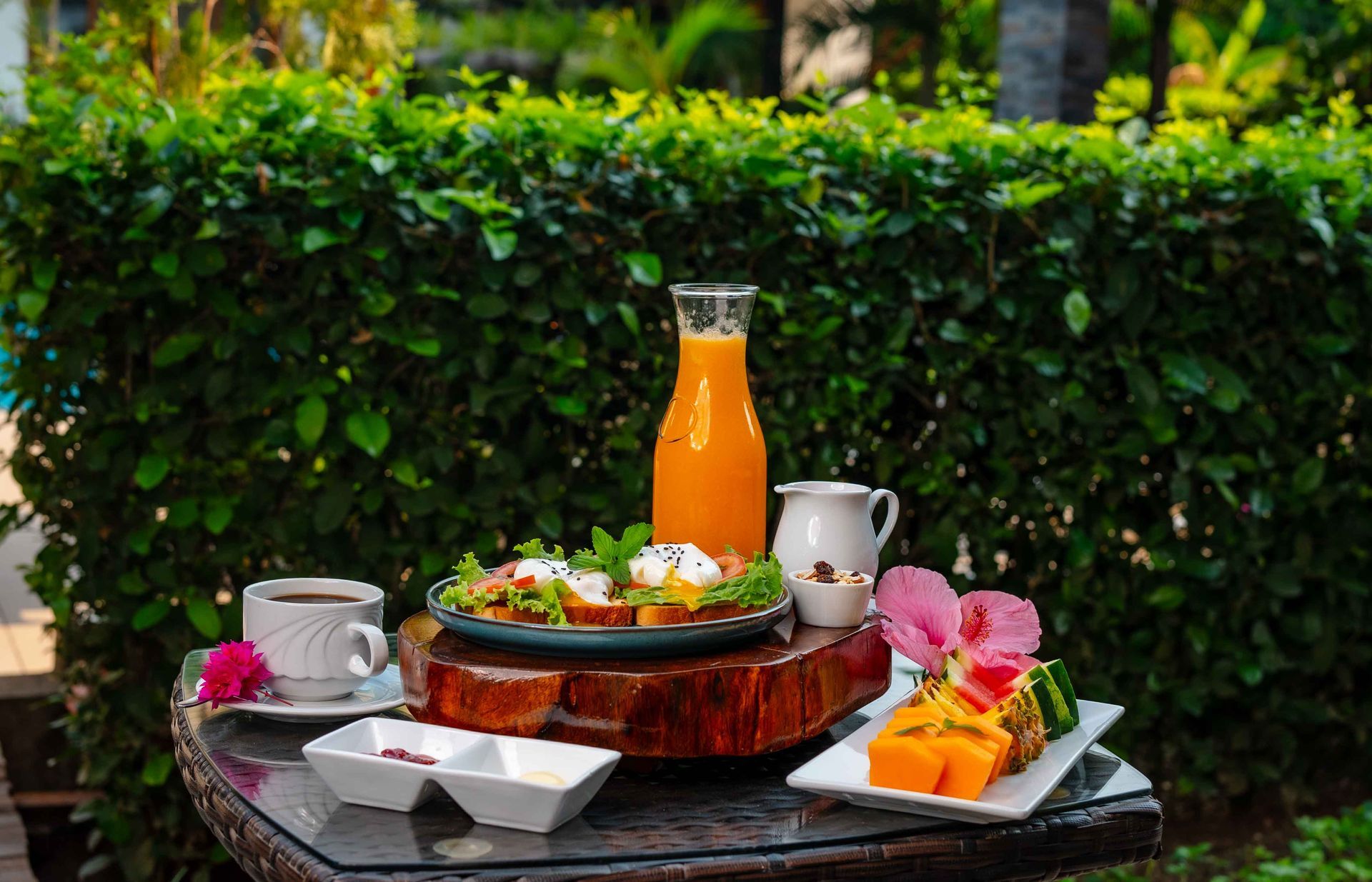Desayuno servido en una mesa al aire libre con zumo, café, frutas y tostadas con huevos escalfados.