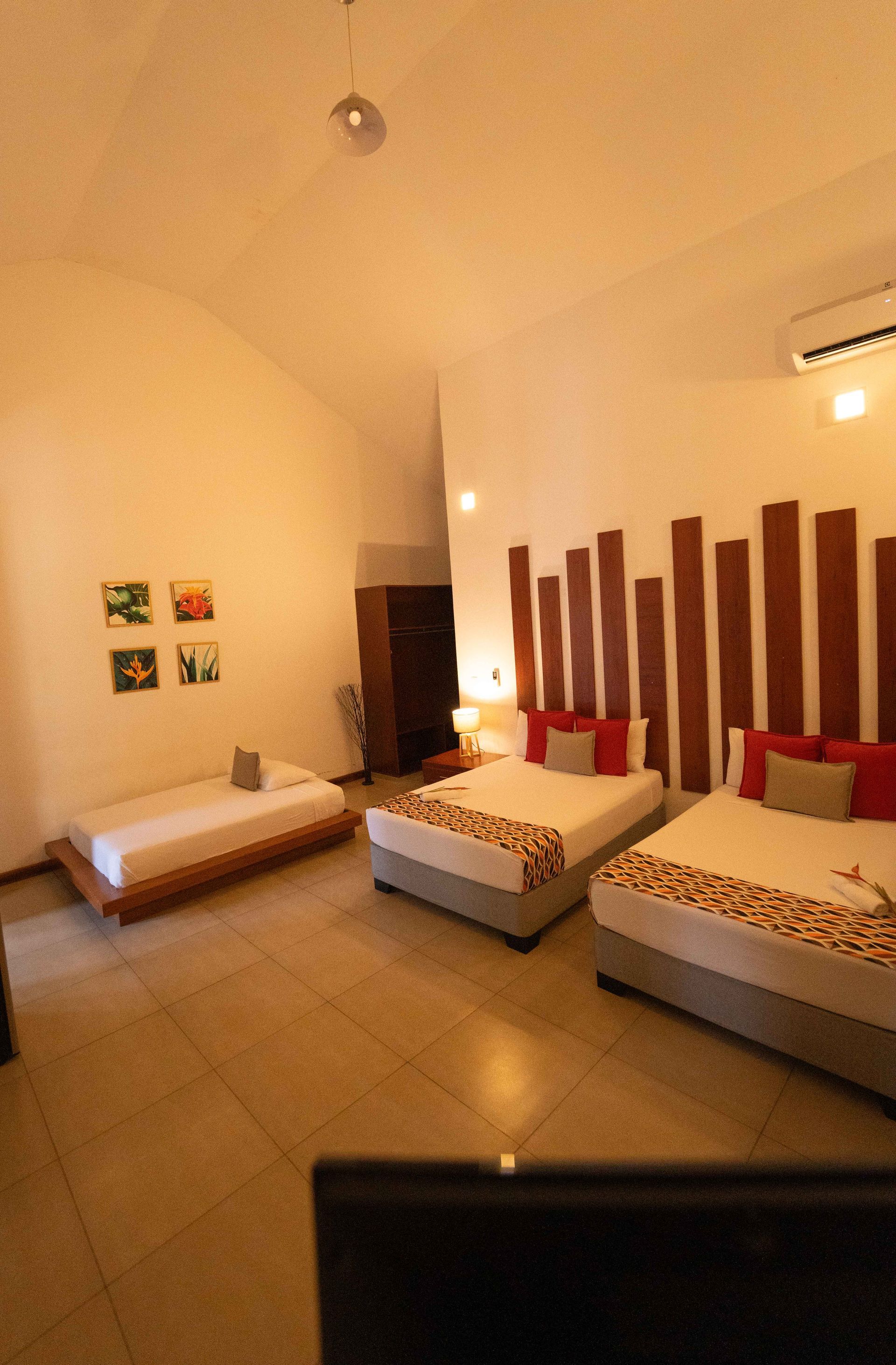 Un dormitorio con tres camas y decoración minimalista de paredes de madera, paredes y pisos de color tostado y luz natural.