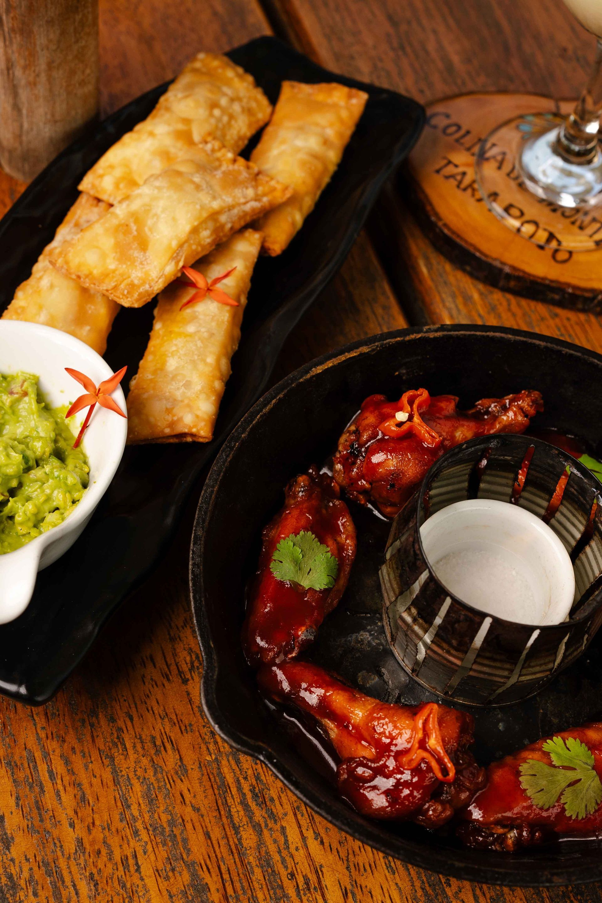 Rollitos de huevo fritos y alitas de pollo con guacamole y salsa sobre una mesa de madera.