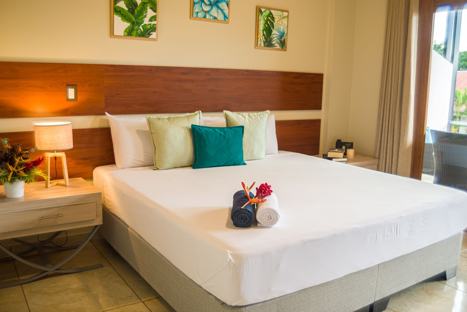 Dormitorio con cama king-size, tonos neutros, almohadas decorativas, obras de arte y puerta al balcón.