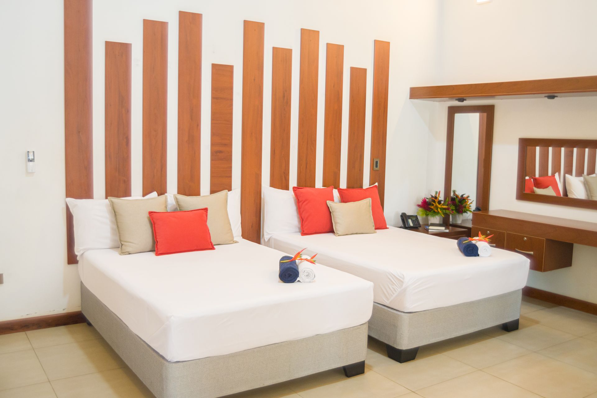 Dos camas individuales con almohadas rojas y beige, cabecero de madera, tocador con espejo.