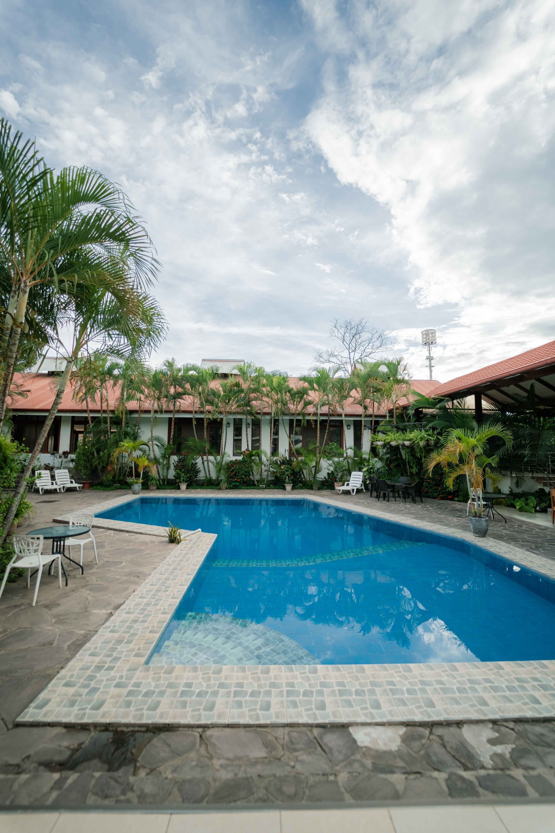 Una piscina rodeada de un edificio y vegetación bajo un cielo nublado.
