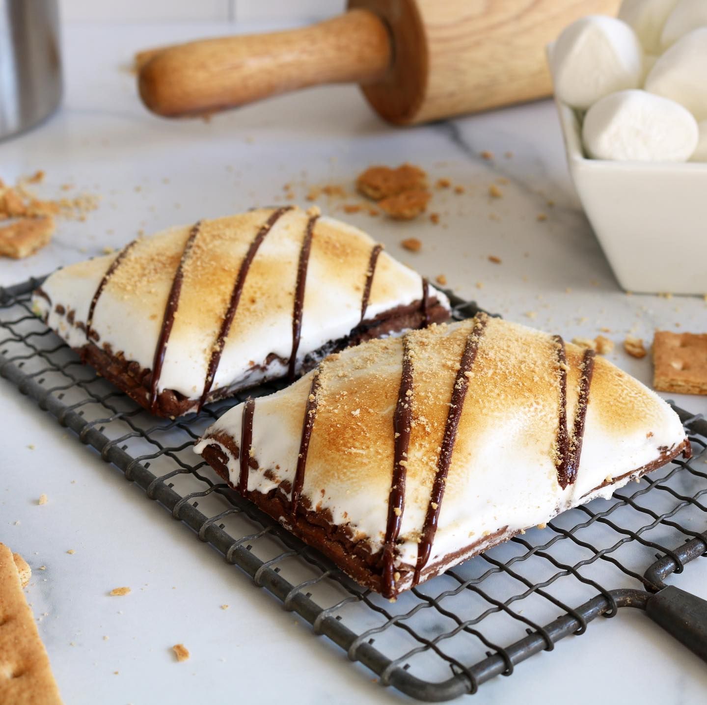 Two s'mores on a cooling rack with a bowl of marshmallows in the background