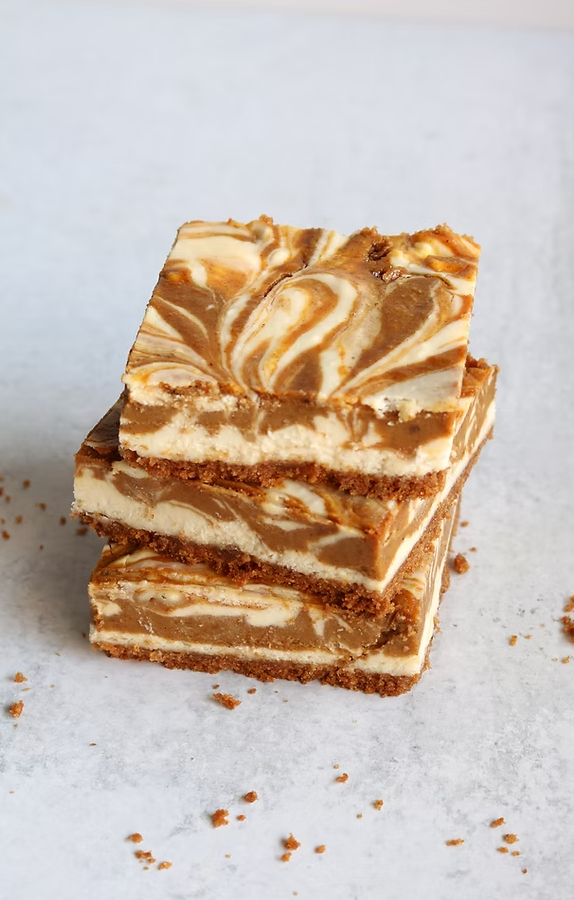 Three cheesecake bars are stacked on top of each other on a white surface.