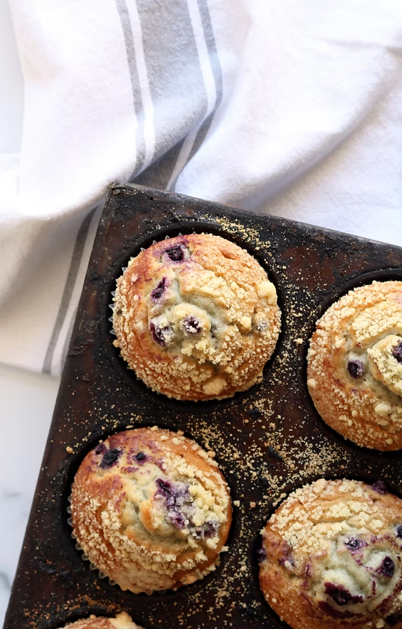 A muffin pan filled with blueberry muffins on a table.