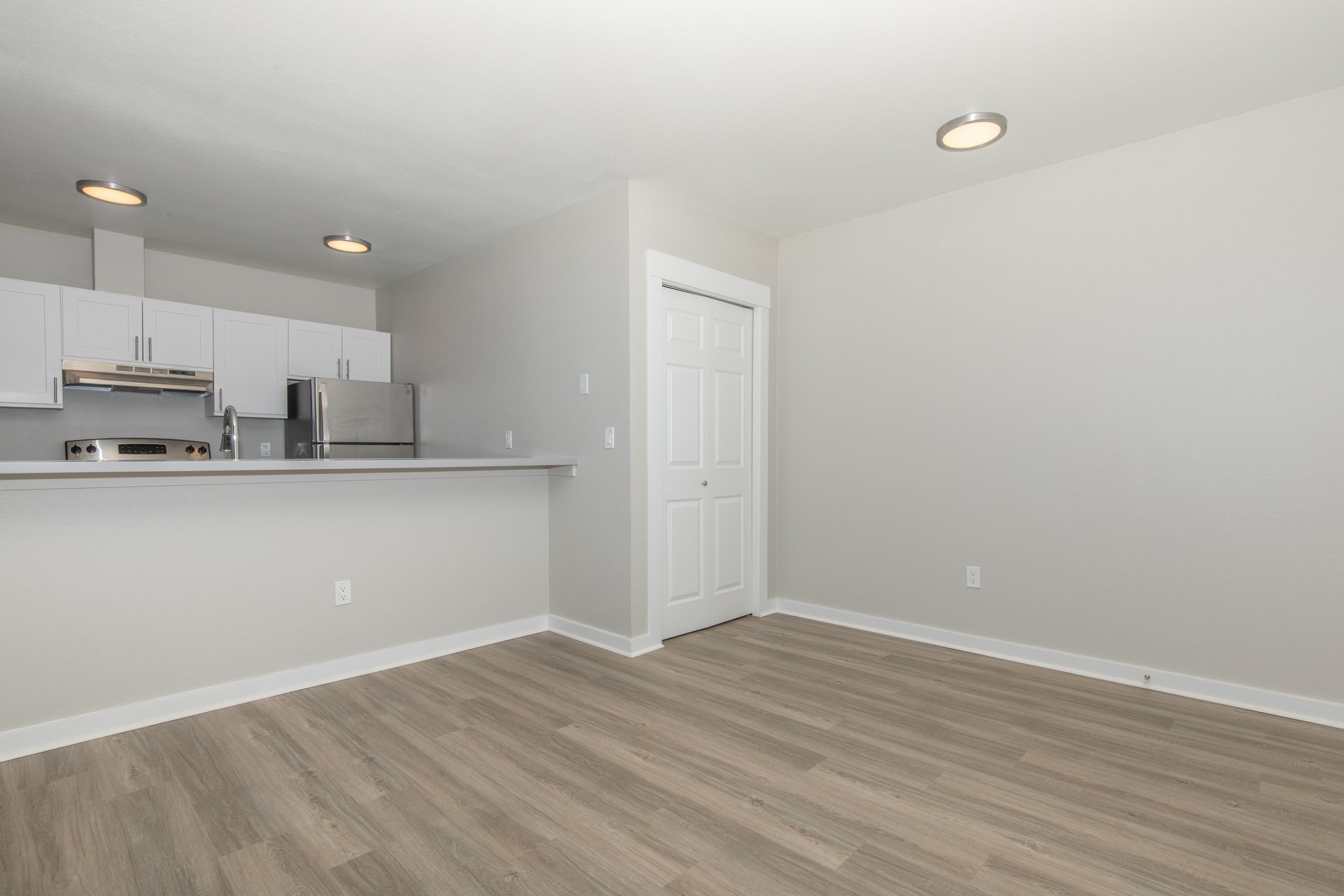 An empty living room with hardwood floors and a kitchen in the background.