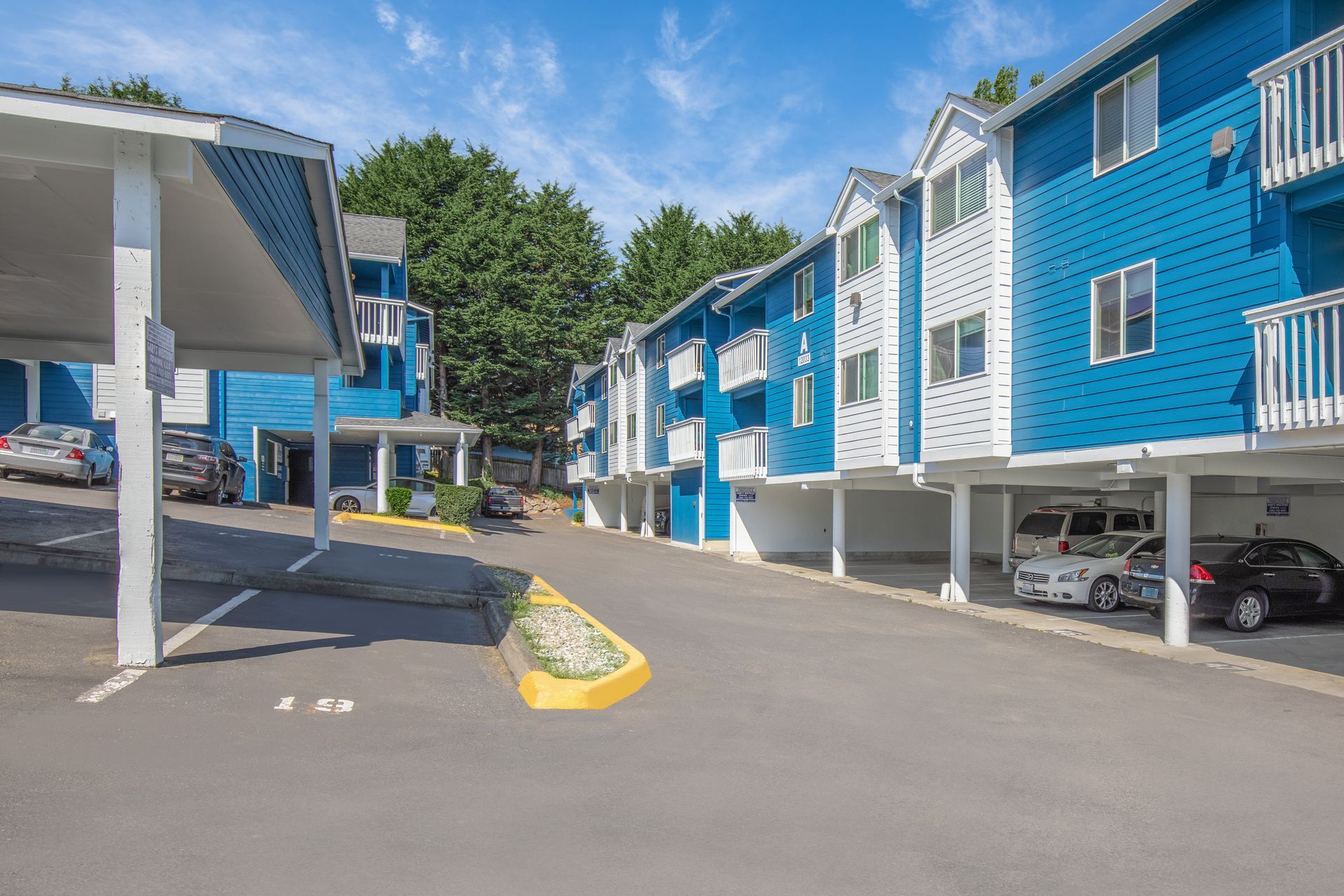 A row of blue and white apartment buildings with cars parked in front of them.