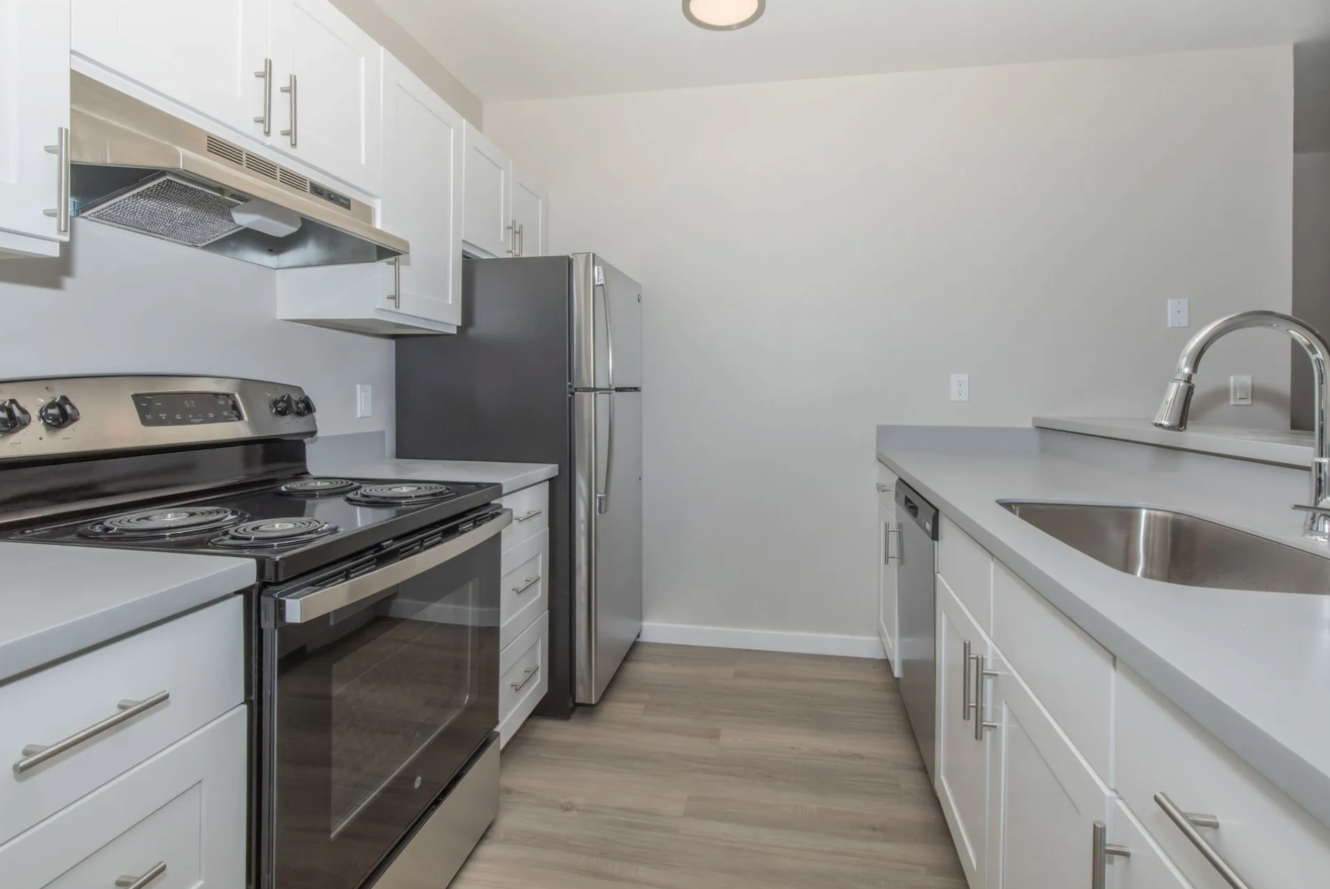 A kitchen with white cabinets , a stove , a refrigerator , and a sink.