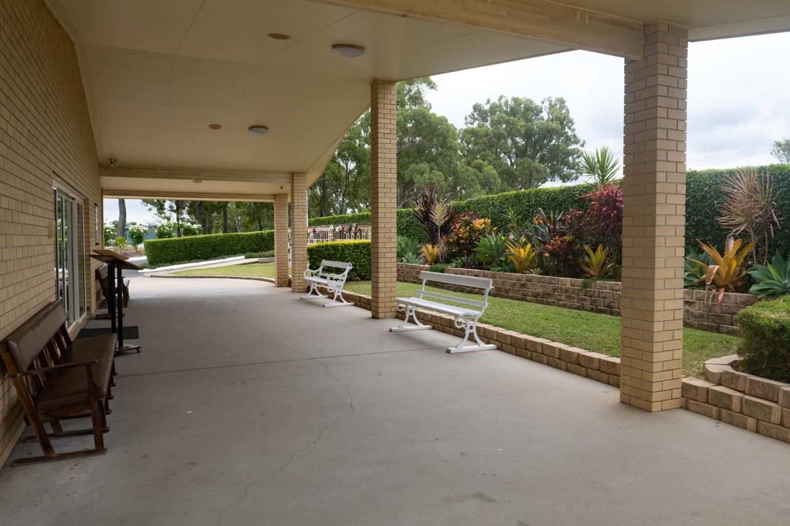 Covered Patio with Brick Pillars, Benches, and A Landscaped Garden in The Background — Rockhampton Crematorium in Norman Gardens, QLD