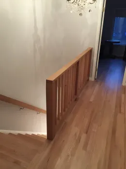 Wooden staircase and railing in a home with light wood floors and white walls.