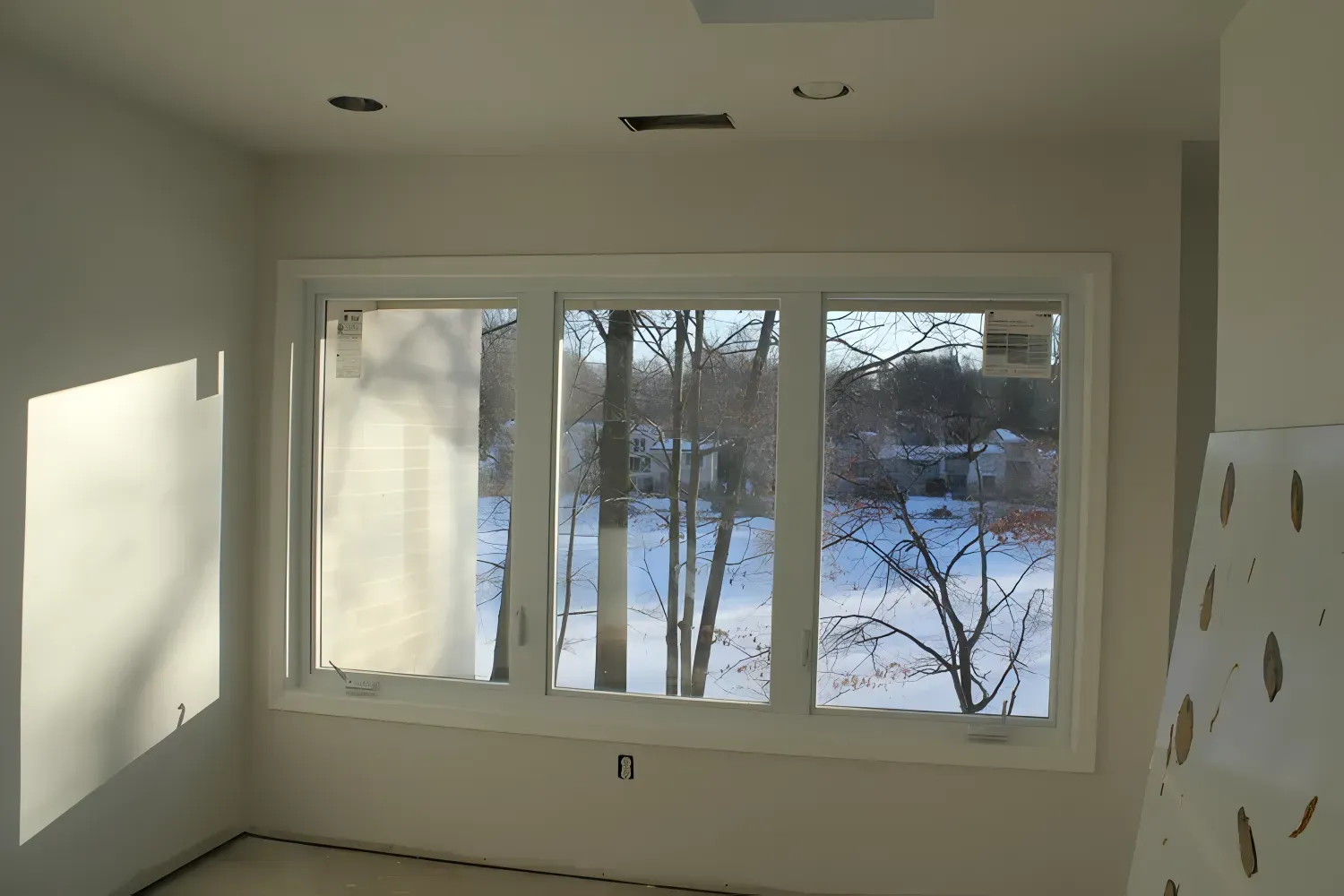 Interior room with a large triple window overlooking a snowy outdoor scene.