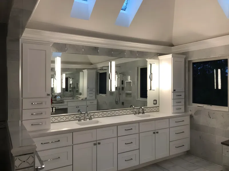 White bathroom with large mirror above double vanity, cabinet storage, and skylights.
