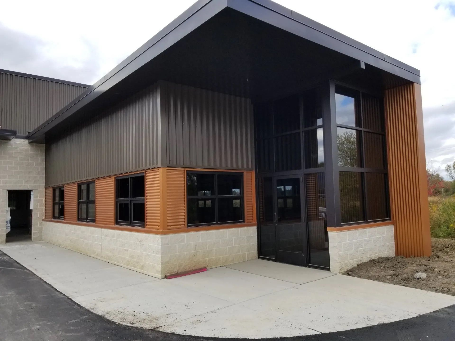 Modern building with brown and black metal siding, large windows, and tan stone base.