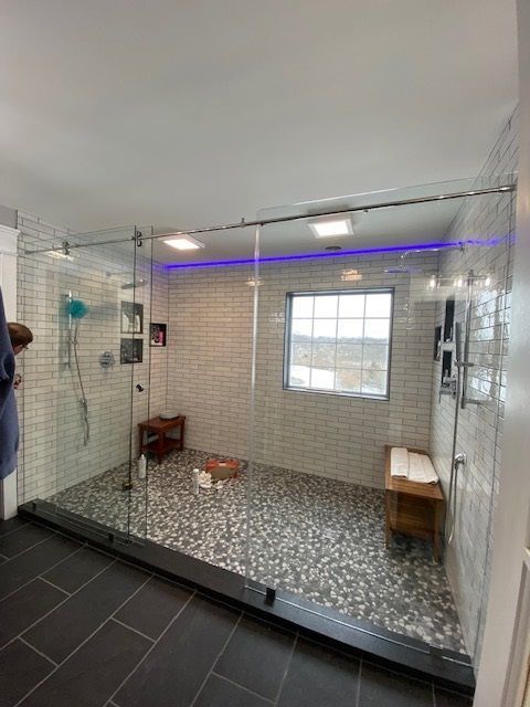 Large, accessible glass shower with pebble floor, benches, and window. Slate-tiled floor outside the shower.