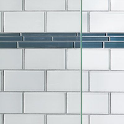 A close up of a white subway tile wall with a blue tile border with glass over top.