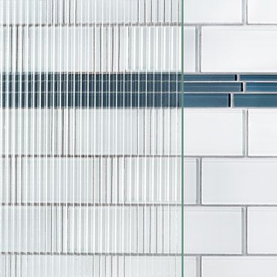A close up of a white subway tile wall with a blue stripe and patterned glass over top.