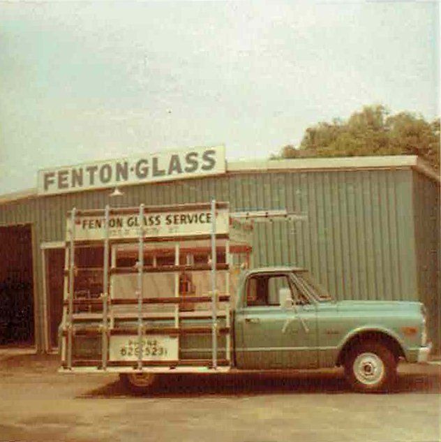 A glass truck is parked in front of a building that says fenton glass
