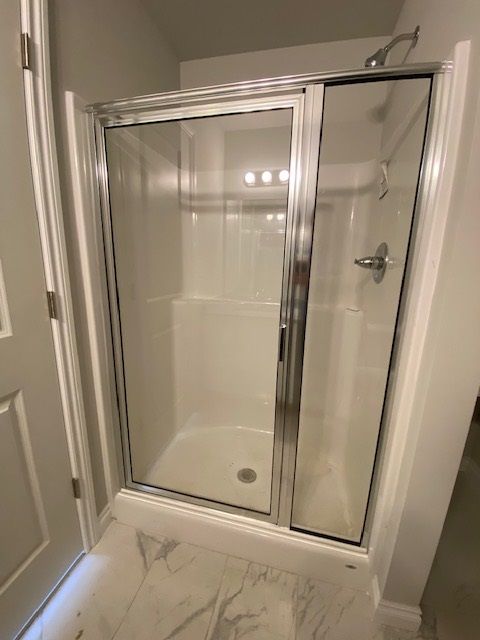 A shower stall with clear glass doors, white interior, and chrome frame. The floor is marble tile.
