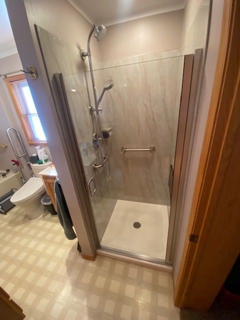Accessible shower with glass doors, grab bar, and handheld shower head in a small bathroom.