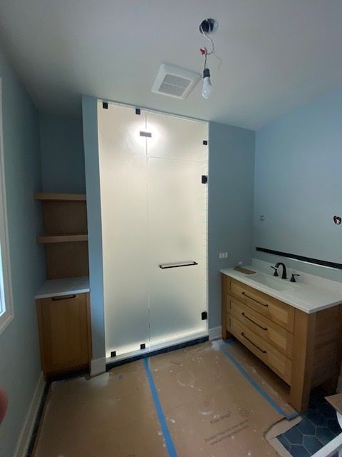 Bathroom with frosted glass shower, wooden vanity, shelving, and light blue walls.