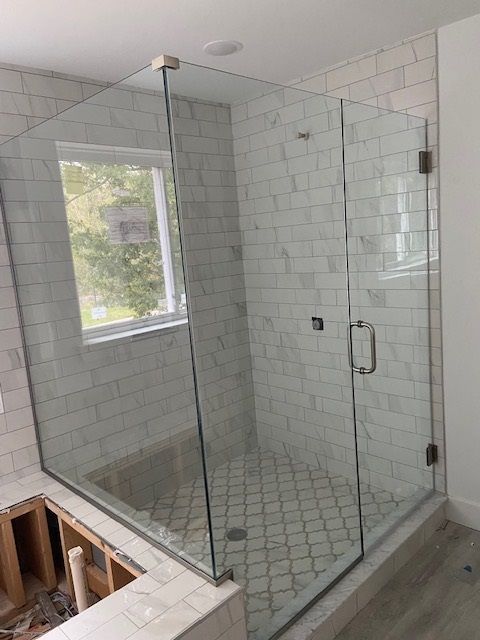 Glass shower enclosure with white tiled walls and floor, and partially built base.