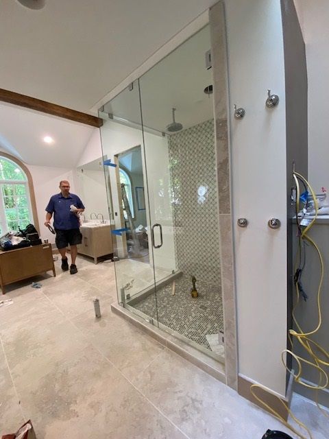 A man in a blue shirt stands in a modern bathroom with a glass shower.