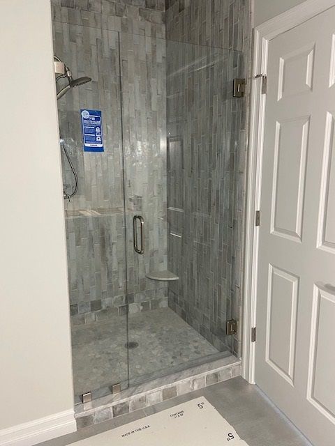 Walk-in shower with gray wood-look tile, glass doors, and a white door to the right.