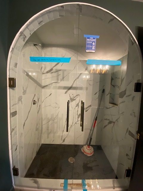 Arched glass shower with marble-look walls, bronze fixtures, and a mop inside.