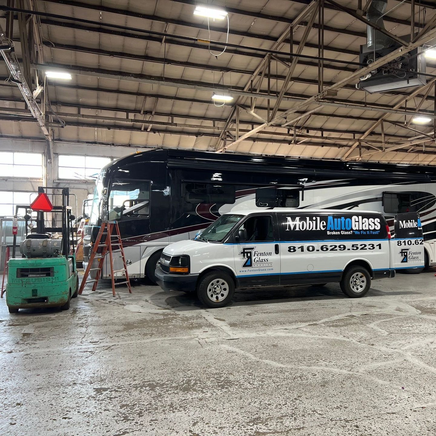 A mobile auto glass van is parked in a garage next to a rv.