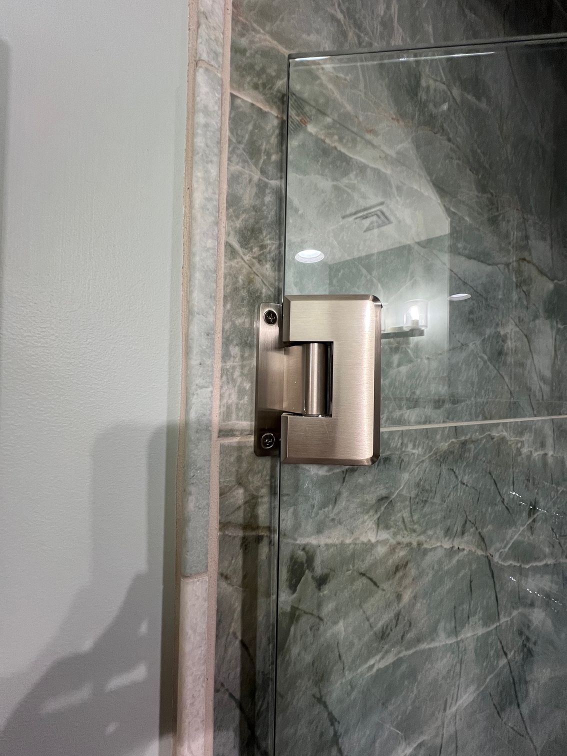 A close up of a shower door hinge on a marble wall.