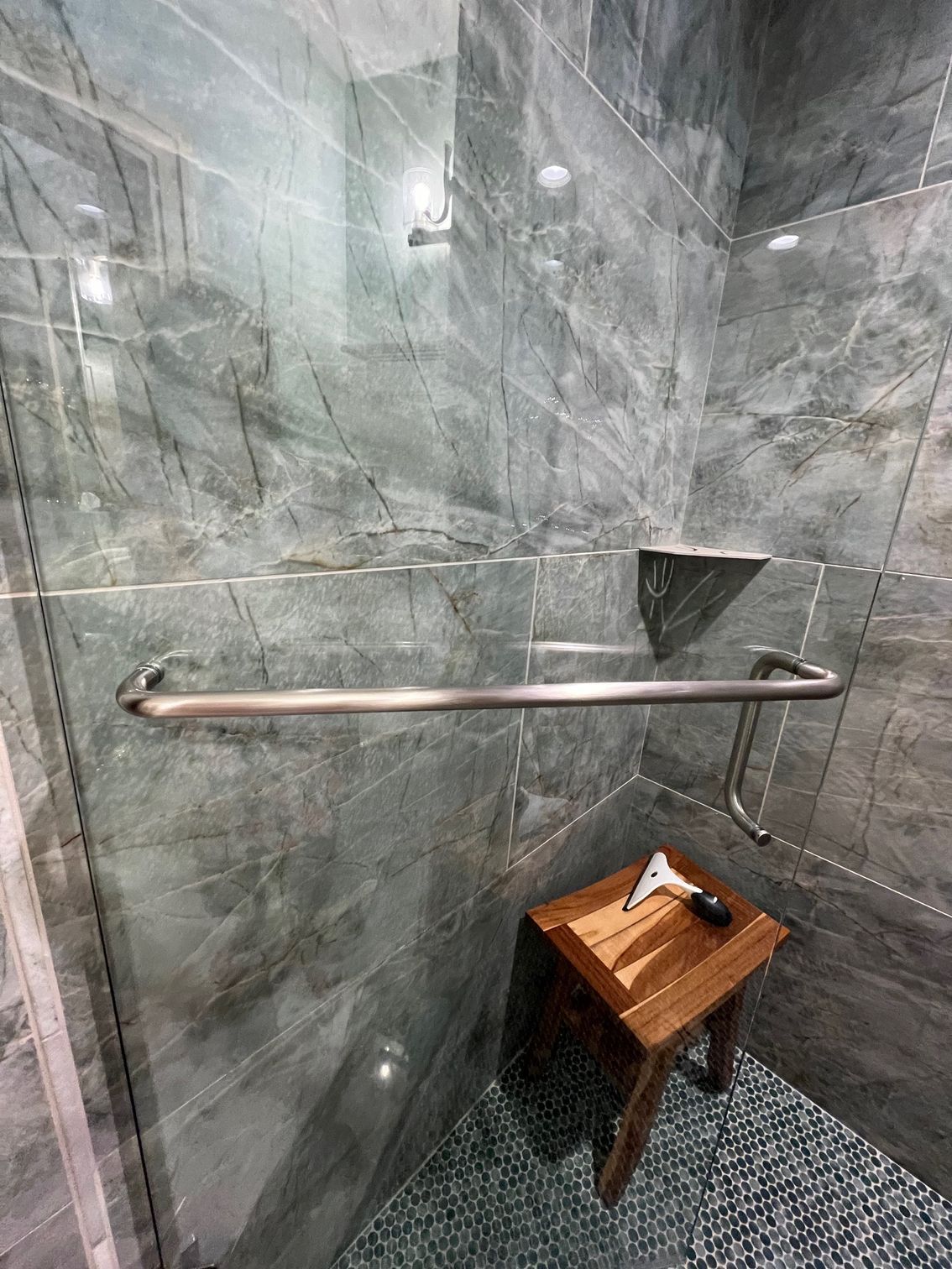 A bathroom with a walk in shower and a wooden stool with a chrome handle.