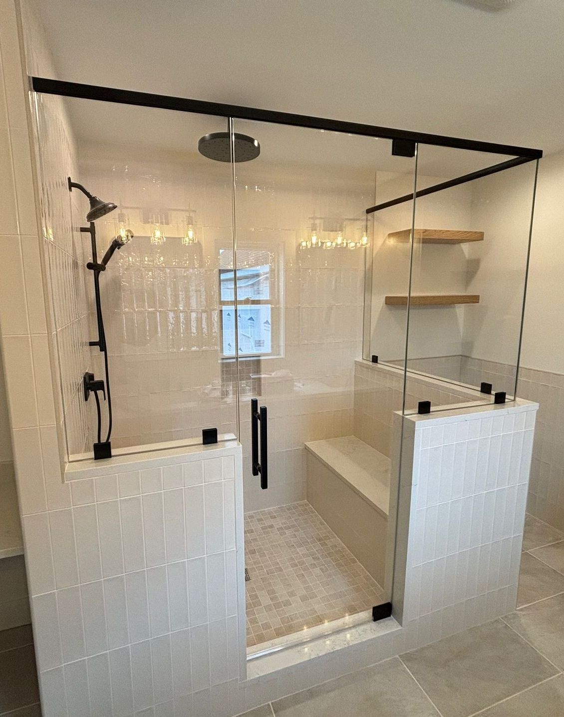 A bathroom with a walk in shower with a glass door and a bench.